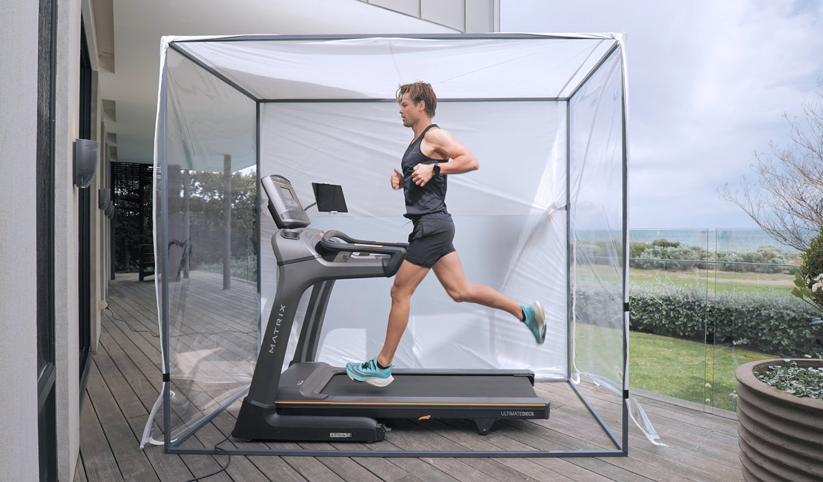 Runner mid-stride on a Matrix treadmill inside the four-poster enclosure, set up on a seaside timber deck