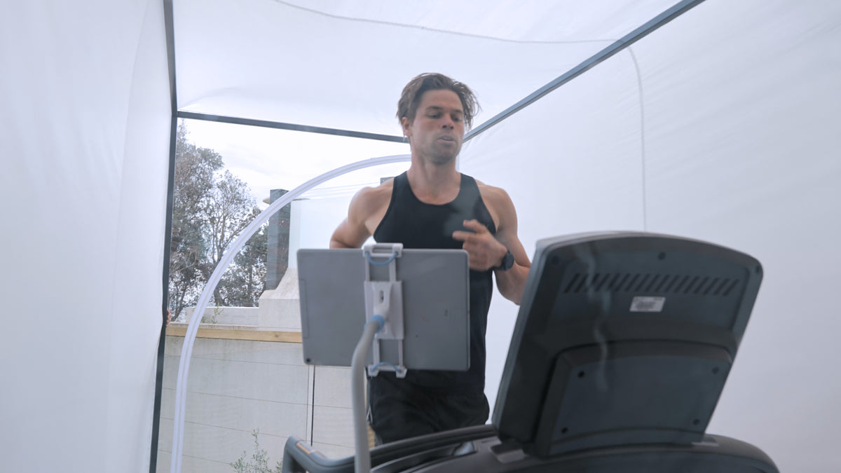 Interior view of a runner on the treadmill, tablet clamped to a stand, white canopy walls either side