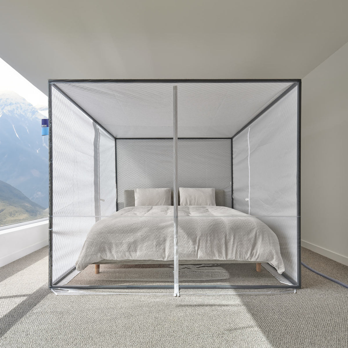 Sleep Cloud altitude tent set up over a made bed in a carpeted bedroom, with a mountain view through the window